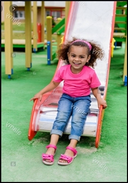 Happy black child sitting at a slide bottom with her feet on the ground